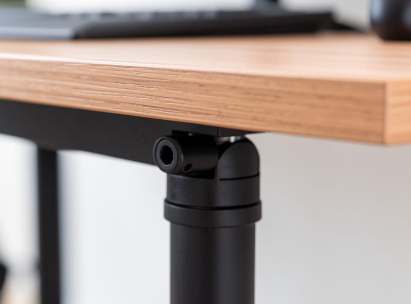Close-up of a compact desk leg joint and a monitor arm clamp biting onto the desk edge