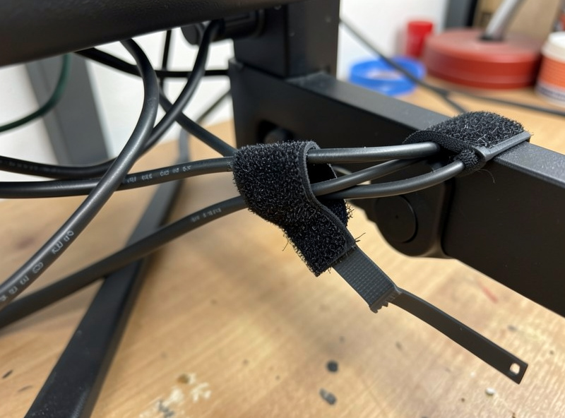 Reusable velcro strap loosely bundling cables on a monitor arm beside a cut zip tie