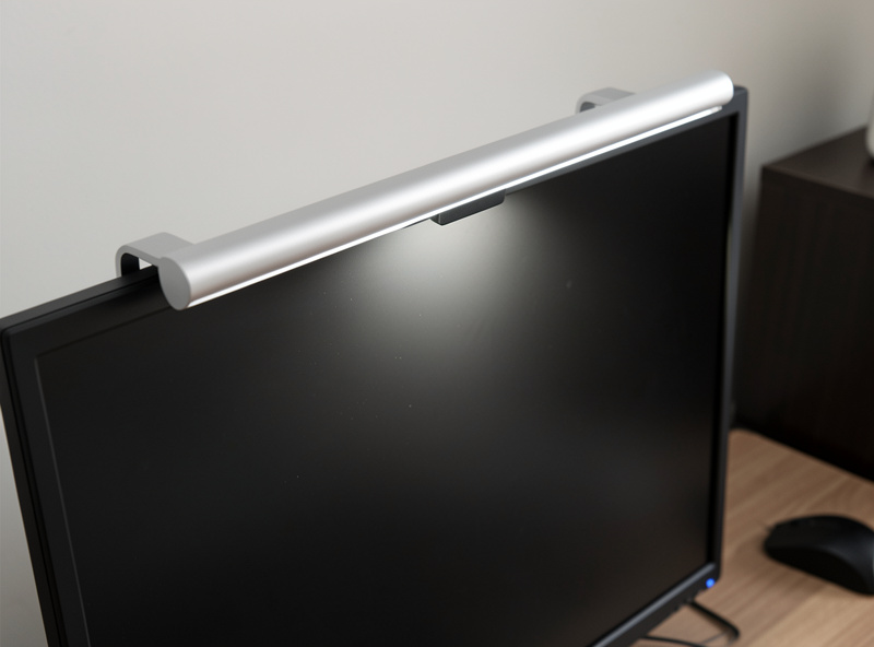 Slim monitor light bar clamped on the top edge of a monitor casting light down onto the desk