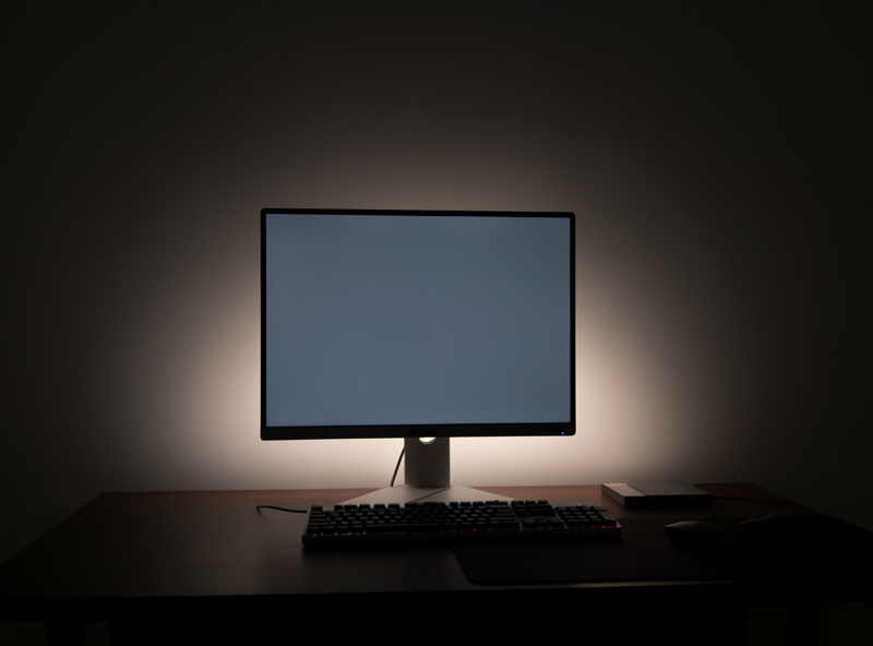LED bias lighting strip behind a monitor casting a soft glow on the wall in a dim room