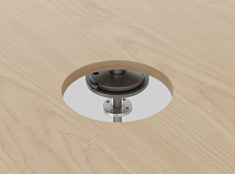 A grommet hole drilled in a desktop with the grommet-mount base of a monitor arm bolted through it
