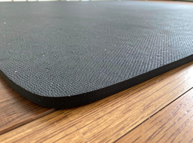 A thick high-density rubber treadmill mat laid under a walking pad on a hardwood floor